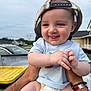 Hayden joined the competition — help win amazing prizes! baby, child, smile, cap, shirt, diaper, tattoo, arm, hand, outdoor, suburban, house, car, cloudy_sky, person, holding, happy, portrait, cute, infant