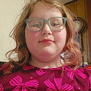 Isabelle is registered to the contest to win money with this photo: child, glasses, disco_ball, pink, maroon_shirt, bows, indoor, wall_clock, hair, face, person, portrait, casual, smile, young, glasses_frame, light, wood_paneling, room, decor