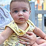Ethan is registered to the contest to win money with this photo: adult_hand, baby, blue_eyes, blurred_background, child, cute, expression, face, hand, holding, infant, onesie, outdoor, person, photography, portrait, rings, sitting, skin, yellow_clothing