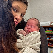 Braxton joined the competition — help win amazing prizes! woman, baby, newborn, sleeping, indoor, striped_clothing, long_hair, holding, face, child, person, toy, books, furniture, shelf, home, cozy, portrait, cute, family