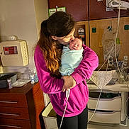 Braxton joined the competition — help win amazing prizes! woman, baby, newborn, hospital, medical_equipment, blanket, pink_hoodie, love, affection, holding, indoor, face, person, sleeping_baby, cabinet, monitor, tubing, hand, care, room