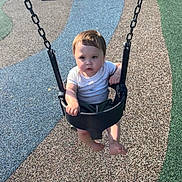 Braxton is registered to the contest to win money with this photo: toddler, child, swing, playground, outdoor, seat, chain, rubber_surface, bench, grass, sunlight, shadow, barefoot, short_sleeve, serious_expression, young_child, daytime, park, play, person