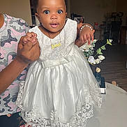 Kaira joined the competition — help win amazing prizes! baby, child, dress, white_dress, lace, hair_accessories, bracelet, necklace, indoor, living_room, adult_hands, flower_vase, table, furniture, portrait, cute, smiling, person, holding, happy