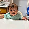 Vera joined the competition — help win amazing prizes! baby, high_chair, smiling, messy, food_stains, kitchen, dishes, clock, wooden_cabinet, face, child, person, indoor, happy, cute, infant, short_hair, green_shirt, table, home