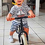 Noah a rejoint le concours — aidez-le/la à gagner de superbes lots ! toddler, child, helmet, balance_bike, indoor, striped_clothing, white_sneakers, smiling, happy, floor_tiles, table, chair, laundry_basket, stairs, home, person, safety_gear, play, toy_bike, casual_clothing