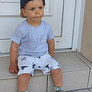 Noah a rejoint le concours — aidez-le/la à gagner de superbes lots ! toddler, child, boy, cap, backwards_cap, shorts, tshirt, sneakers, doorstep, door, concrete, outdoor, serious_expression, sitting, casual_clothing, summer, young_child, portrait, footwear, daylight