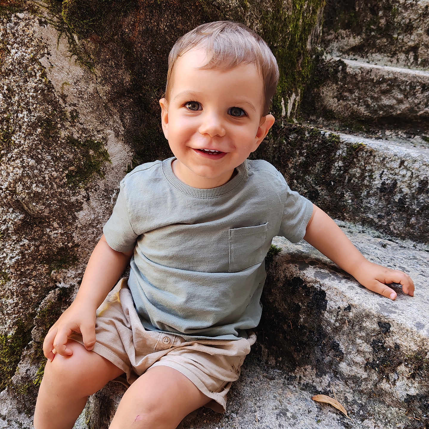 Noah a rejoint le concours — aidez-le/la à gagner de superbes lots ! bare_legs, casual_clothing, child, cute, daylight, happy, moss, natural_light, outdoor, playful, portrait, shoes, shorts, sitting, smiling, stone_steps, stone_wall, toddler, tshirt, young_child