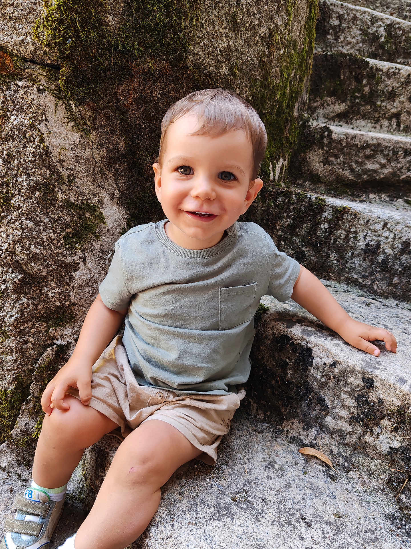 Noah a rejoint le concours — aidez-le/la à gagner de superbes lots ! toddler, child, smiling, sitting, stone_steps, moss, outdoor, casual_clothing, shorts, tshirt, happy, young_child, natural_light, portrait, bare_legs, shoes, daylight, stone_wall, cute, playful