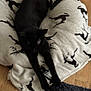 black_cat, cat, stretching, blanket, reindeer_pattern, wooden_floor, indoor, pet, animal, feline, cozy, resting, soft_texture, black_fur, holiday_theme, flooring, domestic, quiet, relaxed, furniture