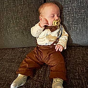 Henry joined the competition — help win amazing prizes! baby, sleeping, pacifier, suspenders, brown_pants, white_shirt, socks, couch, furniture, infant, child, resting, indoors, cute, person, portrait, cozy, soft_lighting, small_hands, relaxed