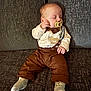 baby, sleeping, pacifier, suspenders, brown_pants, white_shirt, socks, couch, furniture, infant, child, resting, indoors, cute, person, portrait, cozy, soft_lighting, small_hands, relaxed