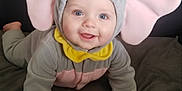 Lennie-Jax is registered to the contest to win money with this photo: baby, blue_eyes, child, crawling, cute, elephant_costume, face, gray_background, hand, happy, hooded_outfit, indoors, infant, pacifier, pink_ears, playful, portrait, smiling, soft_blanket, yellow_hat