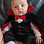 baby, black_clothing, blue_eyes, bow_tie, cape, child, costume, cute, drool, face, hands, indoor, infant, leather, portrait, seat, sitting, socks, vampire, white_shirt