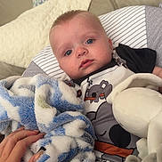 Lennie-Jax is registered to the contest to win money with this photo: baby, infant, blue_eyes, blanket, hand, pillow, koala_print, clothing, striped, couch, indoor, soft_texture, cute, cozy, child, person, laying_down, comfort, nursery, resting