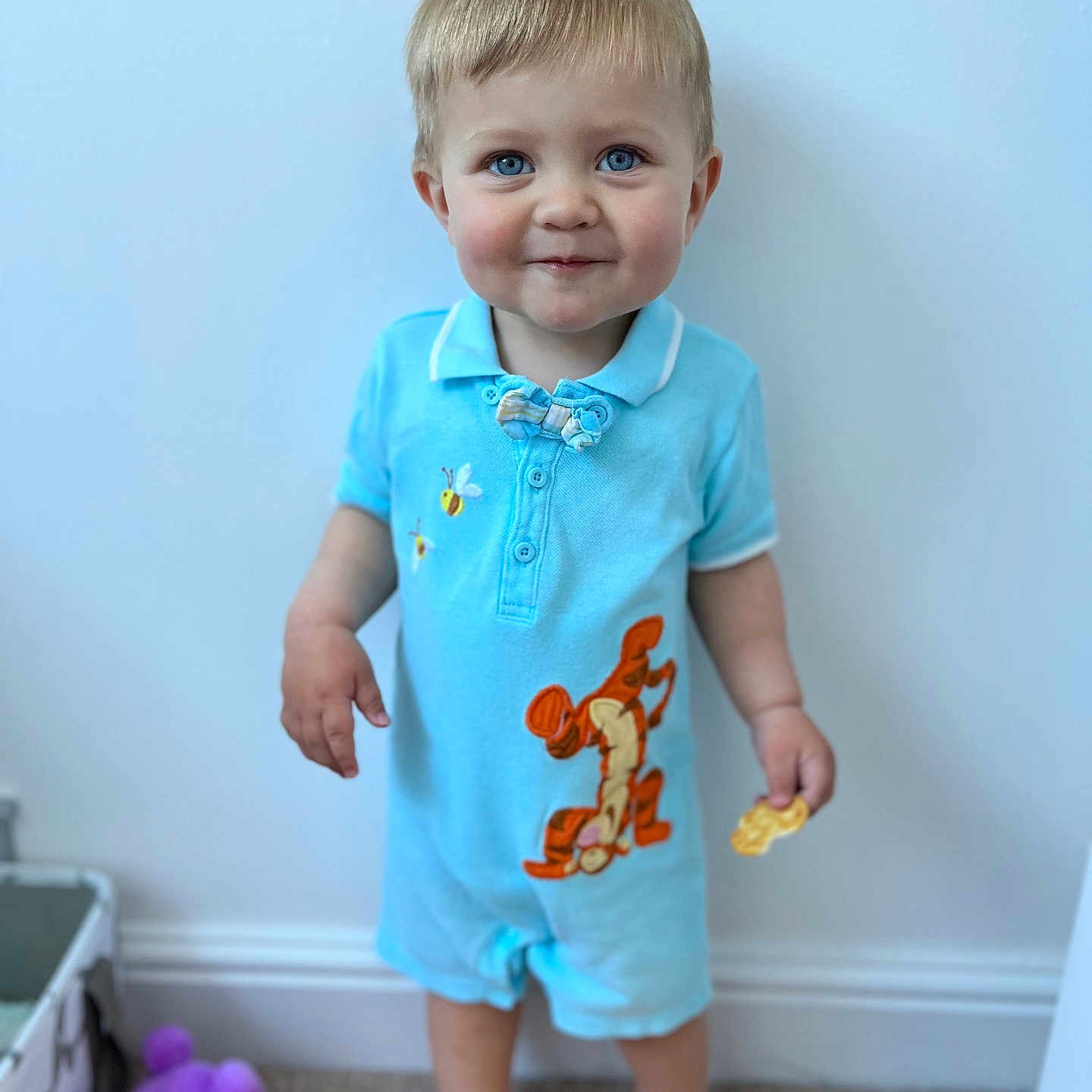 Mason is registered to the contest to win money with this photo: baby, barefoot, blue_eyes, carpet, child, clothing, cute, indoor, light_blue, person, playful, plush, romper, short_hair, smiling, snack, standing, toddler, toy, wall