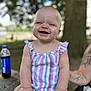 Roselie is registered to the contest to win money with this photo: baby, child, smiling, outdoor, picnic_table, striped_clothing, happy, face, arm, tattoo, bottle, drink, summer, nature, tree, wood, sitting, cute, messy, playful
