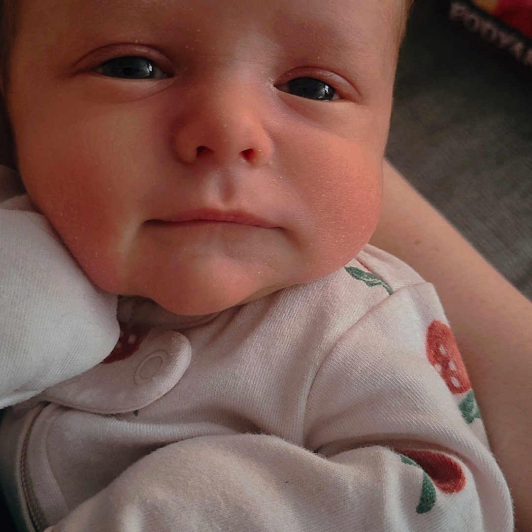 Amira is registered to the contest to win money with this photo: baby, baby_clothes, close_up, clothing, cute, eyes, face, hand, head, indoors, infant, newborn, patterned_outfit, person, portrait, resting, skin, sleepy, soft_light, young_child