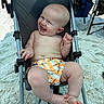 baby, child, smiling, stroller, beach, sand, sunlight, summer, happy, infant, bare_chest, shorts, outdoor, relaxing, cute, person, legs, feet, vacation, playful
