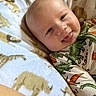 Wylder is registered to the contest to win money with this photo: baby, infant, smiling, tongue_out, dinosaur_print, clothing, blanket, animal_print, cute, happy, face, head, skin, child, lying_down, cozy, soft, young, portrait, indoors