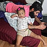 Journèe is registered to the contest to win money with this photo: baby, child, infant, parent, father, family, bedroom, bed, pillow, blanket, sitting, lying_down, smiling, pink_bow, beard, smartphone, tattoo, clothing, wooden_floor, indoor