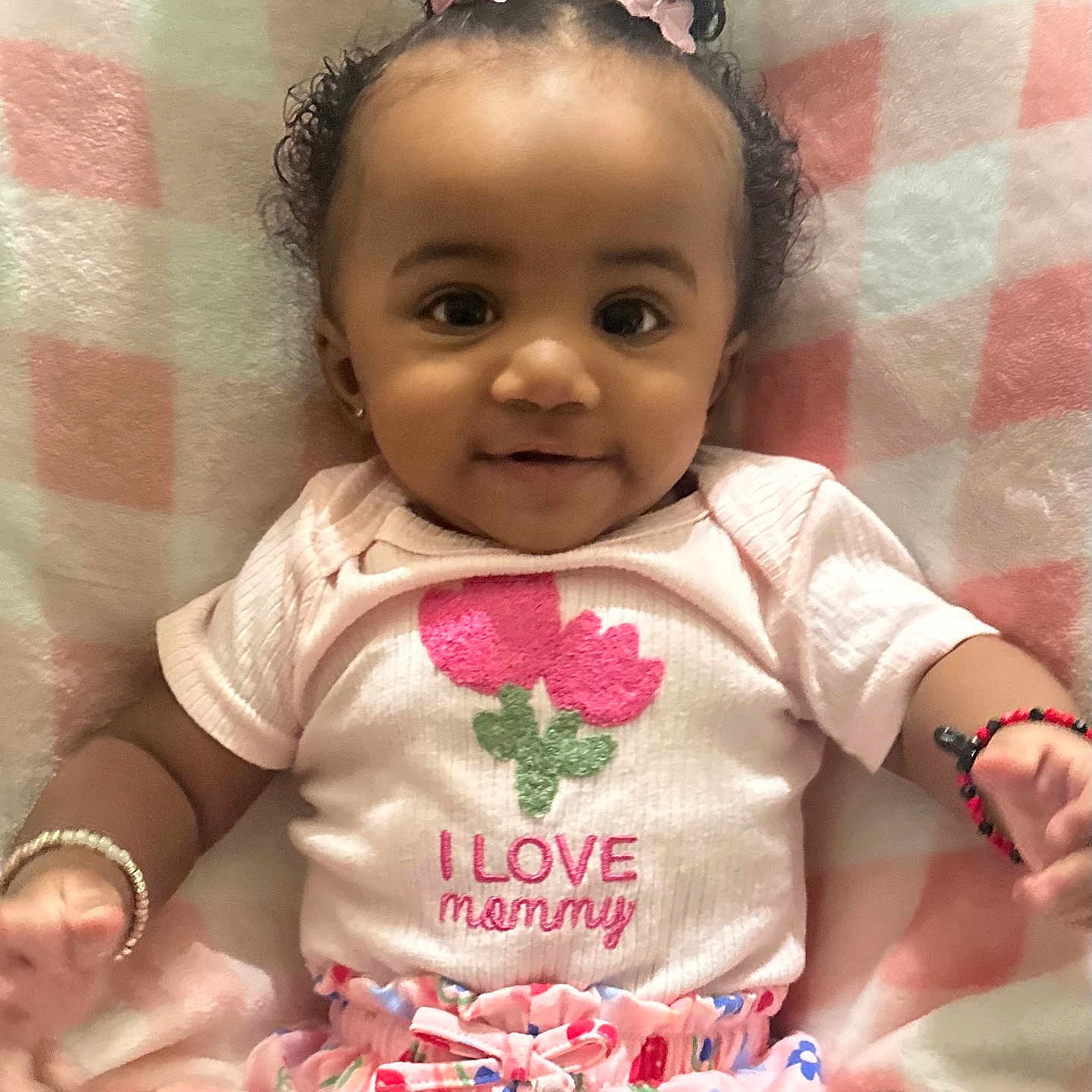 Anayah joined the competition — help win amazing prizes! baby, child, girl, smiling, curly_hair, pink_bows, bracelet, shirt, flower_design, blanket, pink, white, colorful_pants, lying_down, infant, cute, happy, indoors, portrait, adorable