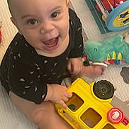 Kalani joined the competition — help win amazing prizes! baby, child, toy, yellow_bus, play_mat, plush_dinosaur, bead_maze, smiling, happy, indoor, floor, clothing, black_outfit, cute, infant, playtime, childhood, expression, person, small