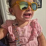 child, toddler, girl, smiling, sunglasses, pink_dress, portrait, indoor, closeup, happy, laughing, face, head, eyeglasses, hair_bow, earrings, pacifier, baby_clothing, family_photo, home_interior