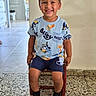 child, boy, toddler, smiling, portrait, sitting, chair, indoor, home, hallway, tile_floor, pajamas, bluey, cartoon, shorts, socks, brown_hair, happy, playful, family_photo