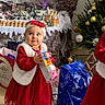 María participe au concours pour gagner de l'argent avec cette photo : black_shoes, bow, child, christmas_bag, christmas_tree, decorations, festive, gift, headband, holiday, indoor, looking_up, miniature_village, ornaments, portrait, present, red_dress, smile, toddler, toy