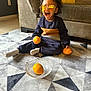 toddler, child, sunglasses, orange, fruit, bowl, rug, carpet, couch, cushion, indoor, living_room, sitting, smiling, happy, curly_hair, clothing, sock, person, home