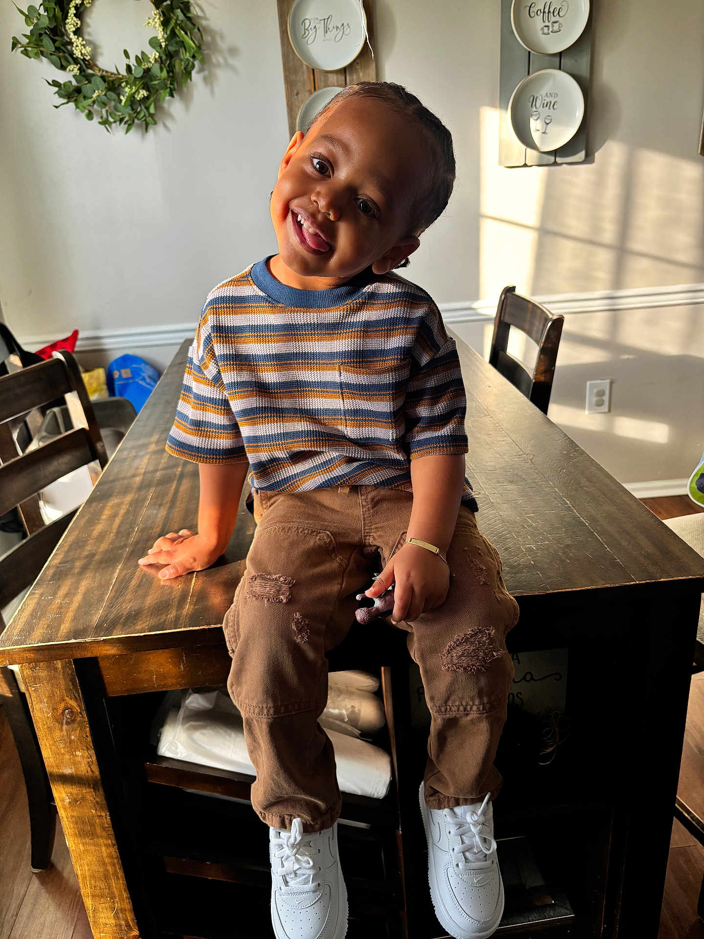 Myles joined the competition — help win amazing prizes! child, toddler, smiling, striped_shirt, brown_pants, white_sneakers, toy, wooden_table, dining_room, chairs, wreath, decorative_plates, sunlight, home_interior, happy, portrait, casual_clothing, playful, indoor, person