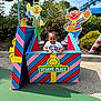 child, smiling, outdoor, sesame_place, colorful, striped_box, bert, ernie, cartoon_characters, playground, greenery, blue_sky, sunny, amusement_park, happy, person, casual_clothing, fun, daytime, toy