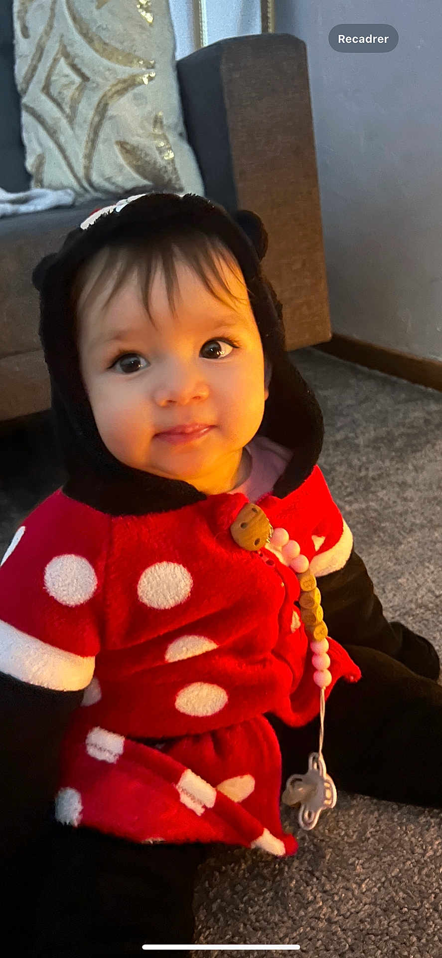 Eline participe au concours pour gagner de l'argent avec cette photo : baby, child, infant, polka_dot, hooded_clothing, pacifier, carpet, indoor, cute, smiling, seated, face, person, black_hair, red_clothing, toy, warm_clothing, home, floor, soft_lighting