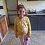 cabinet, casual_clothing, child, decor, door, face, face_paint, home, indoor, kitchen, necklace, person, pink_pants, sink, smile, standing, tile_floor, white_shoes, yellow_sweatshirt, young_girl