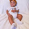 Vienna is registered to the contest to win money with this photo: baby, infant, child, smiling, portrait, lying_down, indoor, blanket, white_blanket, headband, bow, clothing, onesie, cartoon, mickey_mouse, socks, white_socks, happy, face, photography