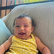 Zoey is registered to the contest to win money with this photo: baby, child, smiling, yellow_clothing, polka_dot, cushion, outdoor, sunlight, happy, portrait, infant, fence, blue_sky, relaxing, cute, skin, face, arm, person, casual