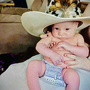 Keegan joined the competition — help win amazing prizes! baby, infant, hat, cowboy_hat, feathers, diaper, person, hand, nail_polish, furniture, couch, living_room, skin, legs, arms, cute, portrait, indoor, holding, seated
