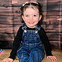 Luna participe au concours pour gagner de l'argent avec cette photo : toddler, child, smiling, denim_overalls, black_shirt, curly_hair, sitting, wooden_floor, wooden_background, portrait, happy, face, person, cute, indoors, young_child, casual_clothing, looking_at_camera, bright_eyes, playful