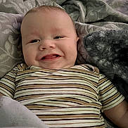 Emmett is registered to the contest to win money with this photo: baby, child, smiling, striped_shirt, blanket, soft_texture, cozy, happy, face, infant, portrait, lying_down, cute, young_child, comfort, home, person, closeup, expression, resting