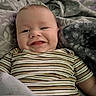baby, child, smiling, striped_shirt, blanket, soft_texture, cozy, happy, face, infant, portrait, lying_down, cute, young_child, comfort, home, person, closeup, expression, resting