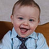 Liam is registered to the contest to win money with this photo: baby, child, smile, tongue, blue_shirt, tie, polka_dot, happy, portrait, indoor, wooden_background, cute, short_hair, sitting, hands, face, person, infant, playful, clothing