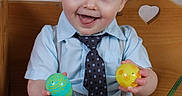 Liam is registered to the contest to win money with this photo: toddler, child, smiling, blue_shirt, tie, suspenders, wooden_bench, heart_cutout, easter_eggs, basket, colorful, happy, indoor, cute, playful, portrait, person, shorts, holding, celebration