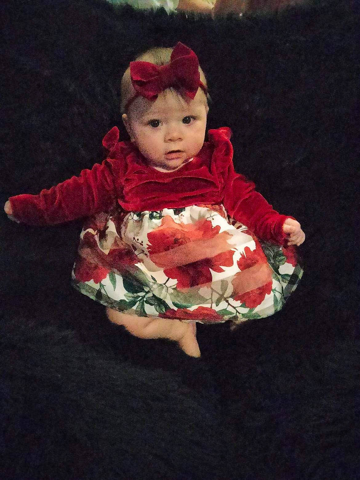 Alyssa is registered to the contest to win money with this photo: baby, baby_products, baby_toddler_clothing, beanie, carmine, child, costume_hat, doll, fur, grass, happy, headwear, human_body, pattern, person, petal, plant, sitting, sleeve, toddler