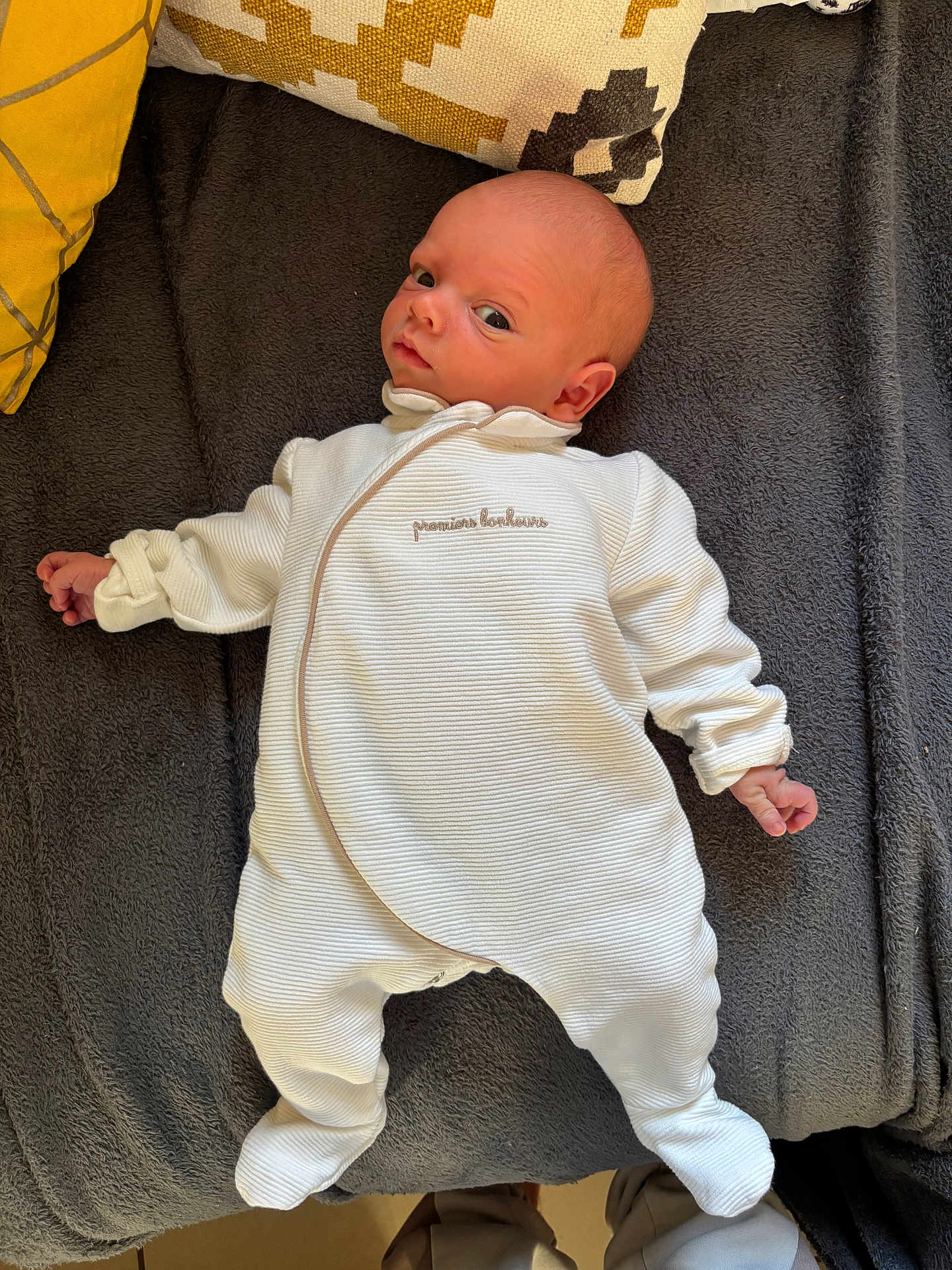 Maécio participe au concours pour gagner de l'argent avec cette photo : baby, infant, white_outfit, blanket, pillow, bed, lying_down, curious, face, head, human, newborn, cozy, indoors, soft_texture, footwear, legs, casual, resting, portrait