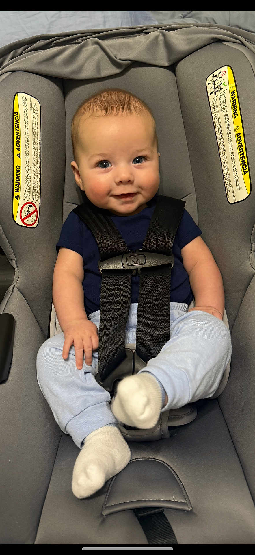 Colton is registered to the contest to win money with this photo: baby, car_seat, child, infant, smile, blue_clothing, white_socks, seatbelt, safety, cute, indoor, person, face, head, young_child, happy, seat, clothing, skin, hair