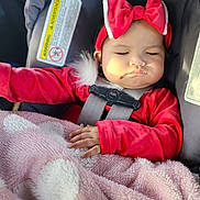 Carlie is registered to the contest to win money with this photo: baby, child, car_seat, red_clothing, headband, bow, blanket, sleeping, closed_eyes, infant, hand, soft_texture, pink_blanket, car_interior, seatbelt, cute, peaceful, portrait, young_child, safety