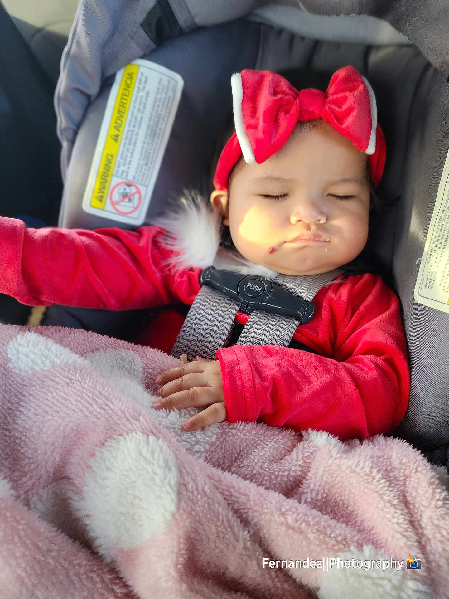 Carlie is registered to the contest to win money with this photo: baby, child, car_seat, red_clothing, headband, bow, blanket, sleeping, closed_eyes, infant, hand, soft_texture, pink_blanket, car_interior, seatbelt, cute, peaceful, portrait, young_child, safety