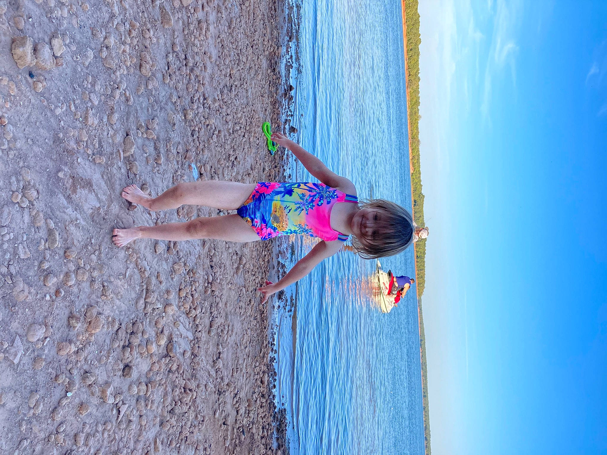 Khloe is registered to the contest to win money with this photo: azure, beach, blue, elbow, electric_blue, fun, happy, human_leg, joy, lake, leisure, ocean, person, plant, recreation, reflection, sky, smile, toddler, tree