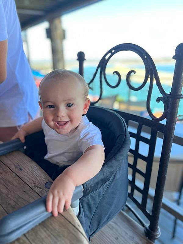 Soren is registered to the contest to win money with this photo: baby, baby_toddler_clothing, child, city, deck, fence, fun, handrail, happy, joy, leisure, ocean, person, recreation, sitting, skin, sky, smile, t_shirt, toddler