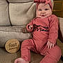 baby, infant, four_months, wooden_sign, headband, bow, pink_outfit, onesie, smile, chubby_cheeks, arm, leg, foot, chair, patterned_fabric, baby_month_marker, sitting, portrait, indoor, baby_gate